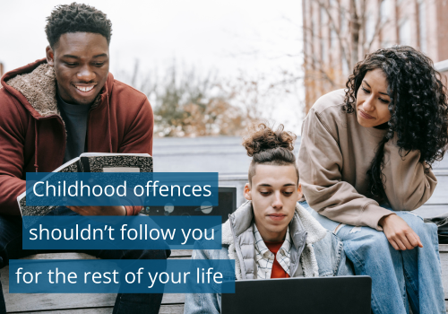 Three young people of different genders and ethnicities are sat outside on a wall. Two are looking at a laptop and one is holding an open notebook, working on something together. Text reads "Childhood offences shouldn